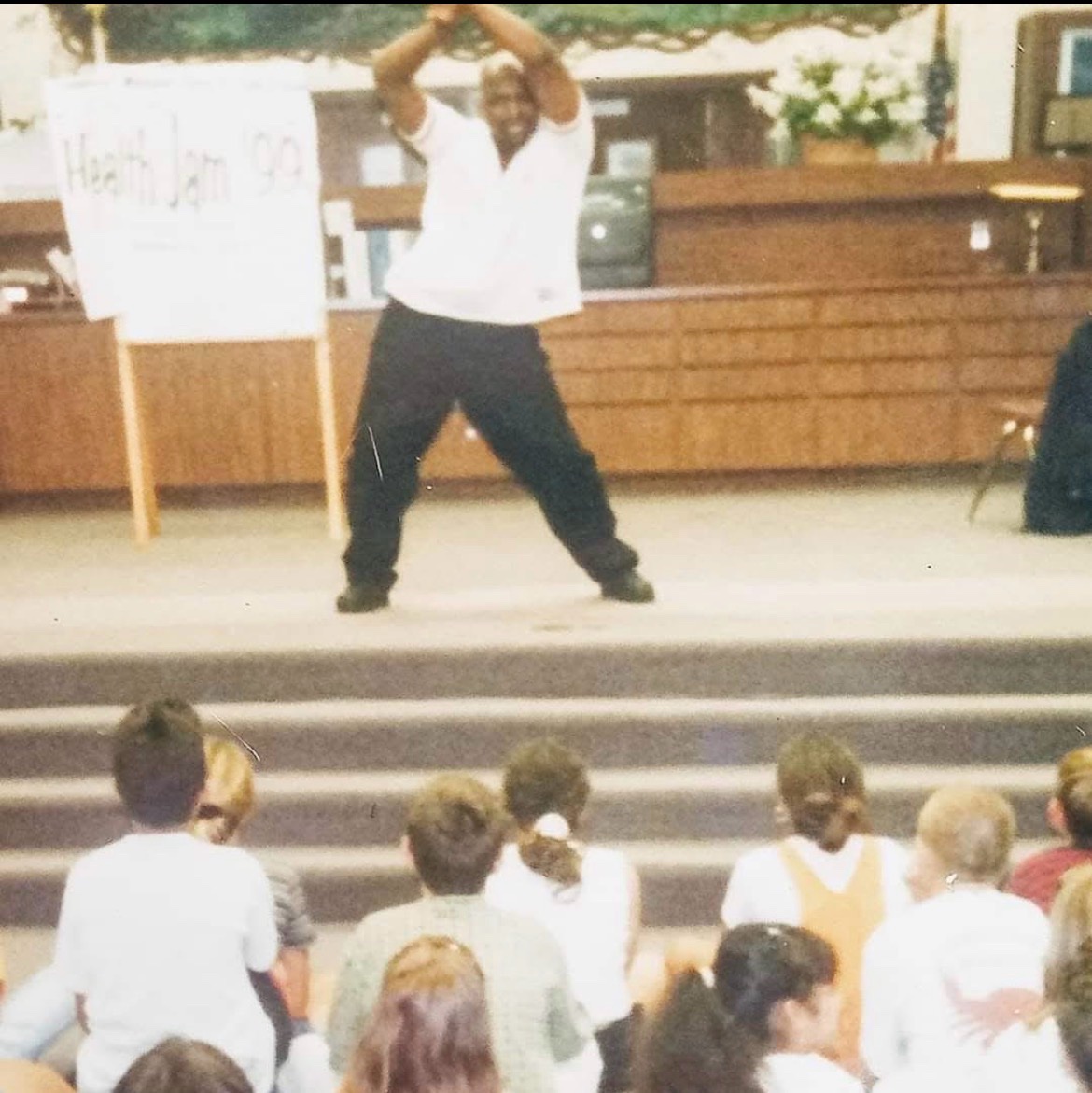 A performer on stage in front of students, beside a sign reading Health Jam ’99